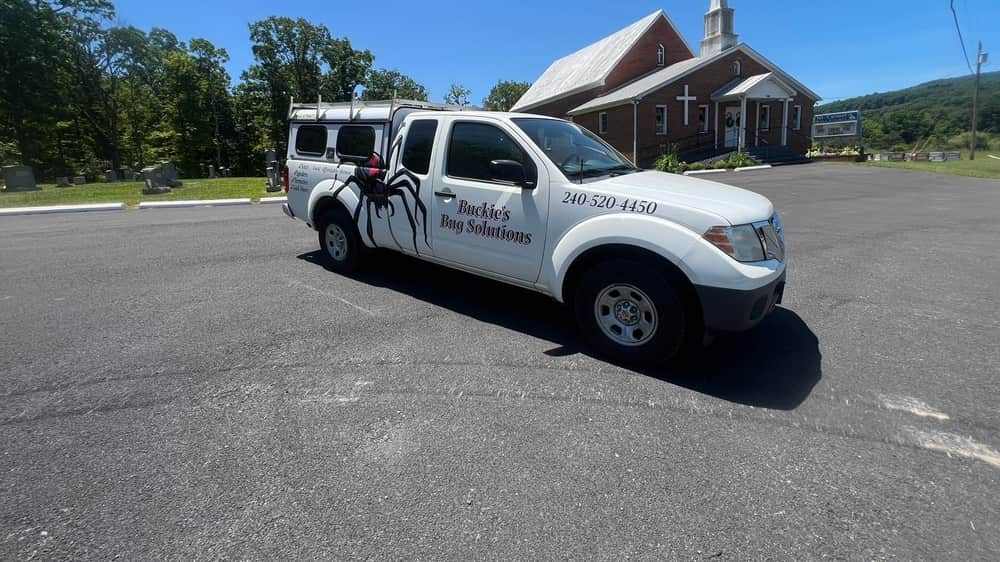 Buckie's Bug Solutions service truck — a white pickup with the black widow graphic — parked outside a church in the Eastern Panhandle