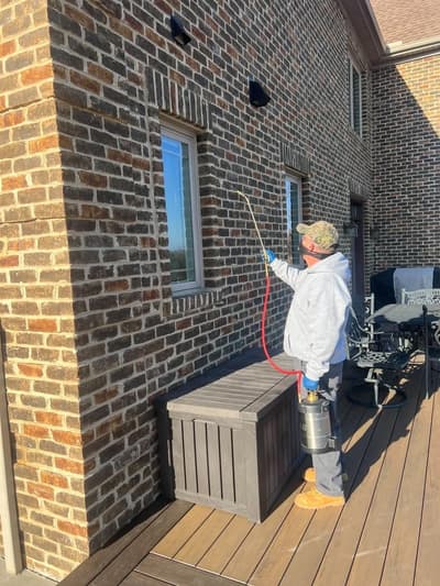 Technician treating the eaves of a brick home with a long extension wand