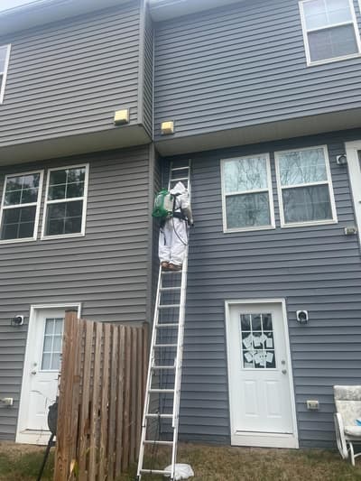 Technician on a ladder treating the upper level of a grey sided house